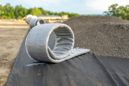 Construction photo of a roll of flat panel drainage pipe being installed on a synthetic turf multi use athletic field. 