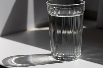 A cut glass of water standing on a white shelf