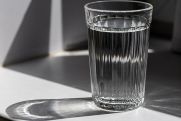 A cut glass of water standing on a white shelf