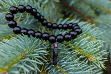 Black beads bracelet with a cross on a fir tree branch