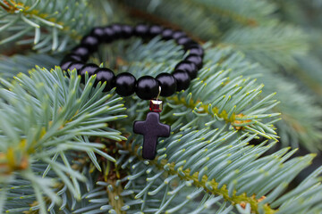 Black beads bracelet with a cross on a fir tree branch