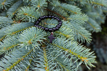 Black beads bracelet with a cross on a fir tree branch
