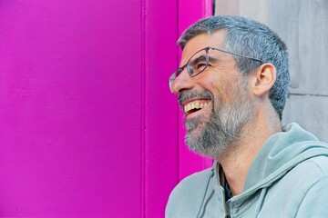 Portrait of a cheerful mature man with grey hair and beard, wearing glasses and a light green...