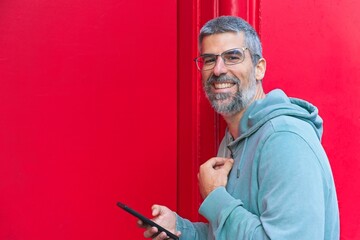 Happy mature man with grey hair and beard, smiling and looking to the camera while using a...