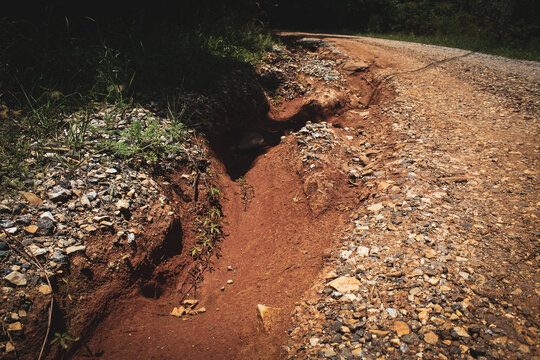 an example of erosion, gully or rill erosion, caused by the movement of water across the red clay soil topped with crushed stone surface
