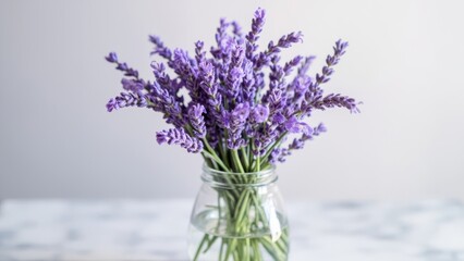 A bouquet of lavender flowers in a clear glass jar sits on a table. The soft, blurred background enhances the vibrant purple hues, evoking a serene and aromatic atmosphere.