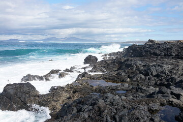 Rugged volcanic coastline with black lava rocks and crashing Atlantic waves. The scene captures the...