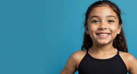 Smiling girl wearing black athletic top against turquoise background. Happy child with brunette hair in sports attire. Youth fitness and active lifestyle concept