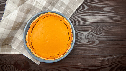 Freshly baked pumpkin pie in a blue ceramic dish, resting on a wooden table, surrounded by a checkered cloth, showcasing a delicious dessert ready for serving and enjoyment