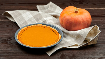 Freshly baked pumpkin pie on a rustic wooden table, accompanied by a whole pumpkin and a checkered...