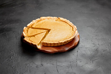 Delicious pumpkin pie on a wooden serving board, with a slice removed, showcasing the creamy filling and golden crust, perfect for autumn celebrations and festive gatherings