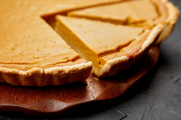 Delicious pumpkin pie with a golden crust, freshly baked and sliced, resting on a wooden board, showcasing a warm and inviting dessert for seasonal celebrations