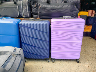 Colorful luggage pieces, including a blue suitcase and a purple suitcase, are arranged together, showcasing various textures and patterns in a travel setting with bags in the background