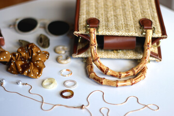 Wicker purse, sunglasses, scrunchie, lipstick and various gold and neutral jewelry on white background. Selective focus.