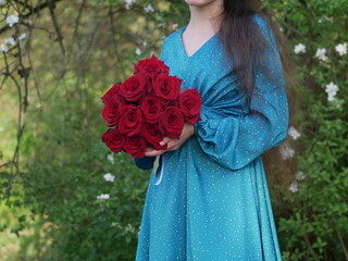 Women hold red roses in hands. Fantasy girl in a blue dress holding red roses.