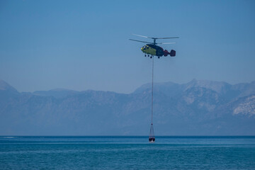 Firefighting helicopter drawing water from the sea to extinguish the forest fire