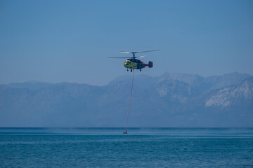 Firefighting helicopter drawing water from the sea to extinguish the forest fire