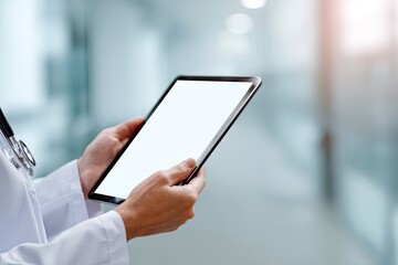 Close-up of a doctor's hands holding a tablet computer with a blank white screen, set against a blurred hospital hallway backdrop
