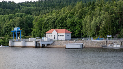 Small hydropower dam with a technical building and blue crane installation, surrounded by dense...