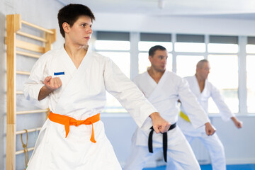 Focused beginner young judo fighter in kimono standing in attacking stance, practicing punches or...