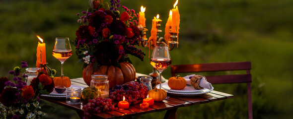 Cozy autumn table decoration for a thanksgiving party outdoors. Grapes, fig, rose wine, candles, pumpkins as decor. Elegant wedding fall arrangement, beautiful setting for a romantic proposal