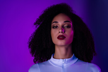 Portrait of a fashionable young woman with curly hair against a vibrant purple background,...