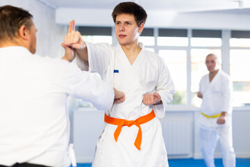 Obraz premium Concentrated young guy in kimono honing punching techniques during kumite with male opponent at karate training session