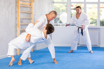 Men of different ages train to make throws on the mat under the guidance of a judo coach