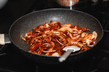 Sliced onion with paprika powder in a pan, fried on a gas stove, with a visible spatula, in natural light