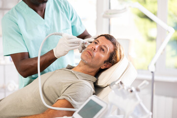 Male cosmetic doctor meticulously performs cosmetic procedure on another man, utilizing hydrogen...