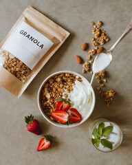 Yogurt being spooned onto granola with fresh strawberries, a healthy breakfast setup from above.
