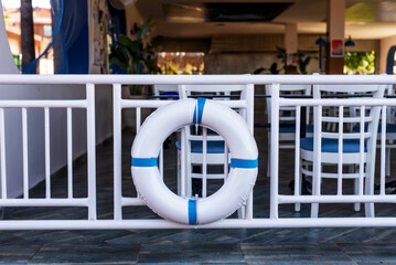 Blue and white lifebuoy on railing in outdoor cafe with white chairs and blue decor