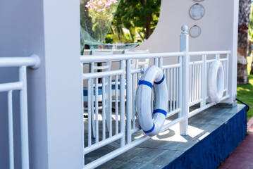 White lifebuoy on blue and white balcony by garden with greenery