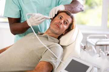 Obraz premium Adult man receiving facial cleansing with ultrasonic shovel to enhance efficacy of skincare products and improving skin texture. Modern hardware cosmetology and male grooming concept