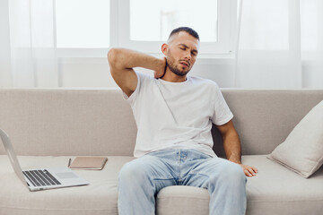 A stressed man sitting on a couch, experiencing work-life blur, showcasing anxiety and fatigue from...