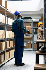 Inventory system managed by african american worker in safety gear, checking the cargo boxes on the...