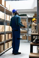  Inventory system managed by african american worker in safety gear, checking the cargo boxes on the racks. Storage units hold packages and containers for delivery, import export. © DC Studio
