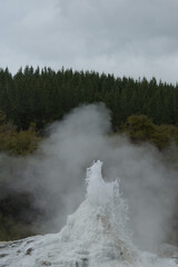 A powerful geyser erupts with a towering column of steam and water, set against a misty, dramatic...