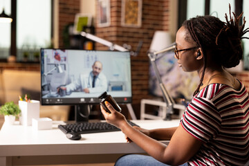 African american woman seated at desk talking to caucasian doctor on video call. Black female...