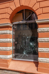 A damaged window on the ground floor of a building with an orange facade and white decor