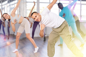 Obraz premium Positive young man and group of multinational active sports people in sports clothes performing rock and roll dance in modern