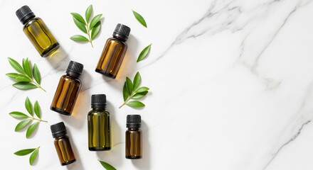 Essential oil bottles with green leaves on marble surface