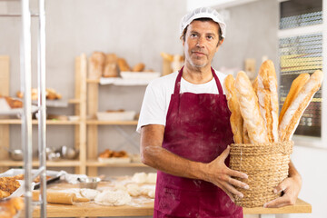 Caucasian man baker with basket of baguettes, shows goods. He has made large number of fresh...