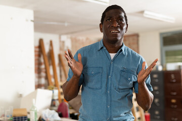 Emotional upset and worried african american houseowner standing in old cluttered house in need of...