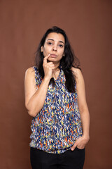 Contemplative woman standing with thoughtful expression, touching her chin and pondering an answer....