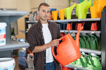 Young man shopper choosing watering can in gardening department of hardware store