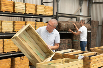 Mature male customer chooses wooden box in store. Man inspects wooden box for storing garden...