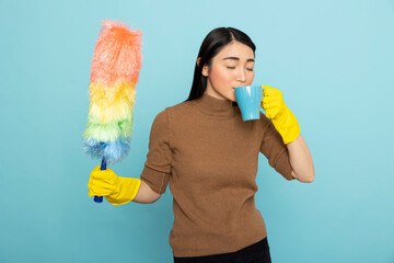 Asian housekeeper holding colorful duster and drinks coffee while taking a break during spring...