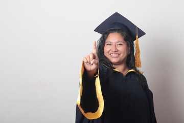 Young brunette Latina woman wearing a cap and gown celebrates her graduation and the completion of...