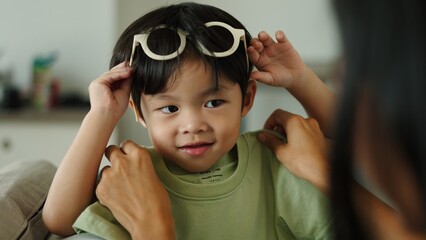 Mother dressing her son and putting sunglasses on him